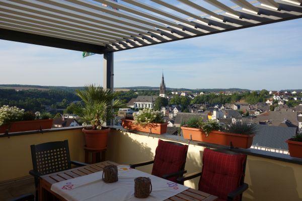 Gemütliche Terrasse mit Sitzgruppe, Blumen und Panoramablick auf eine idyllische Kleinstadt.