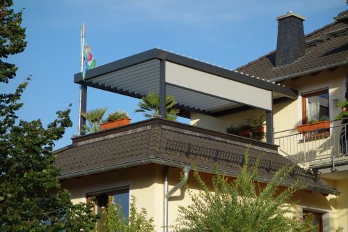 Moderne Terrasse mit Lamellendach und Pflanzen auf einem Balkon eines Einfamilienhauses.