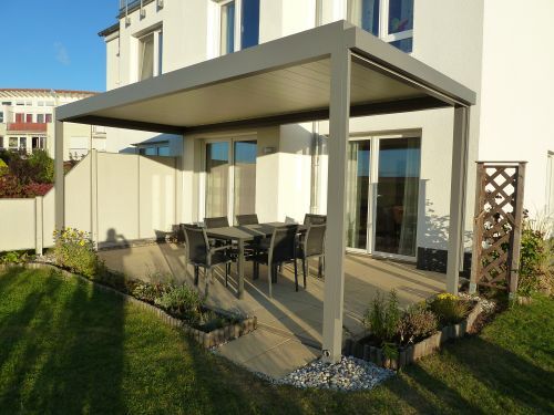 Moderne Terrasse mit Überdachung und Gartenmöbeln an einem Einfamilienhaus im Sonnenschein.