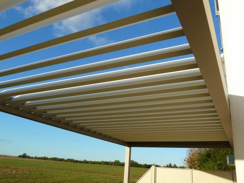Moderne Terrassenüberdachung aus Aluminium mit Lamellendach vor blauem Himmel.