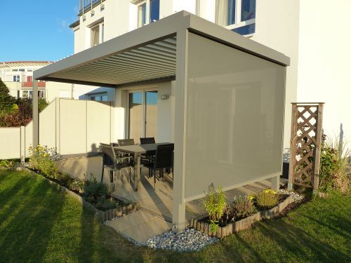 Moderne Terrassenüberdachung mit Sonnenschutz und Gartenmöbeln an einem Einfamilienhaus.