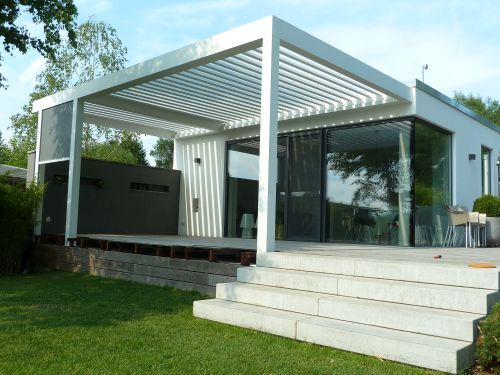 Modernes Haus mit großer Glasfront und stilvoller Terrasse mit Lamellendach im Garten.